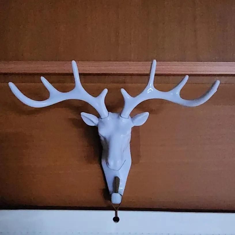 The Gir Farmer white self adhesive coat hook shaped like a deer head mounted on wooden wall