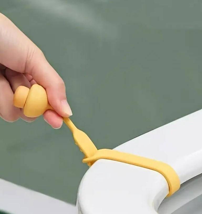 Hand using a yellow hygienic toilet lid lifter to lift a white toilet seat lid