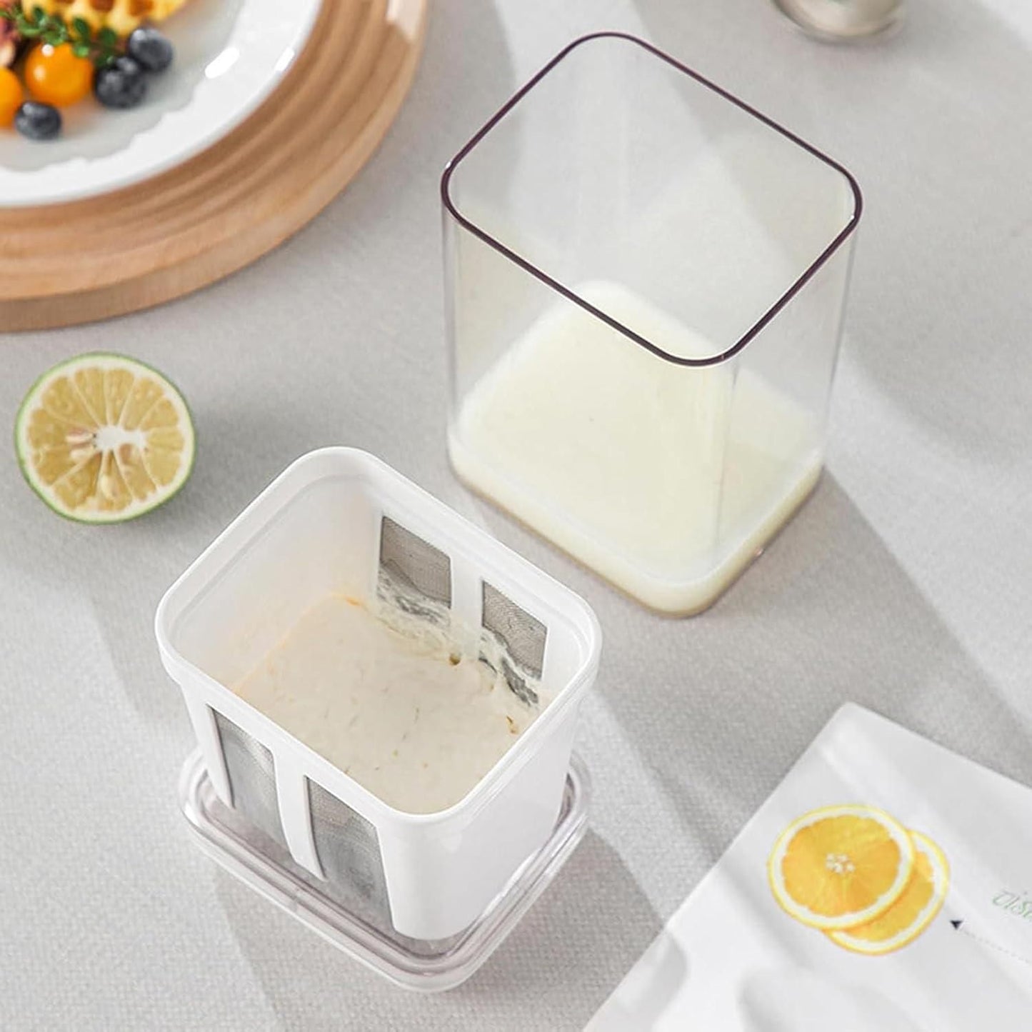 White yogurt maker with strainer placed on table with fresh fruit and ingredients nearby