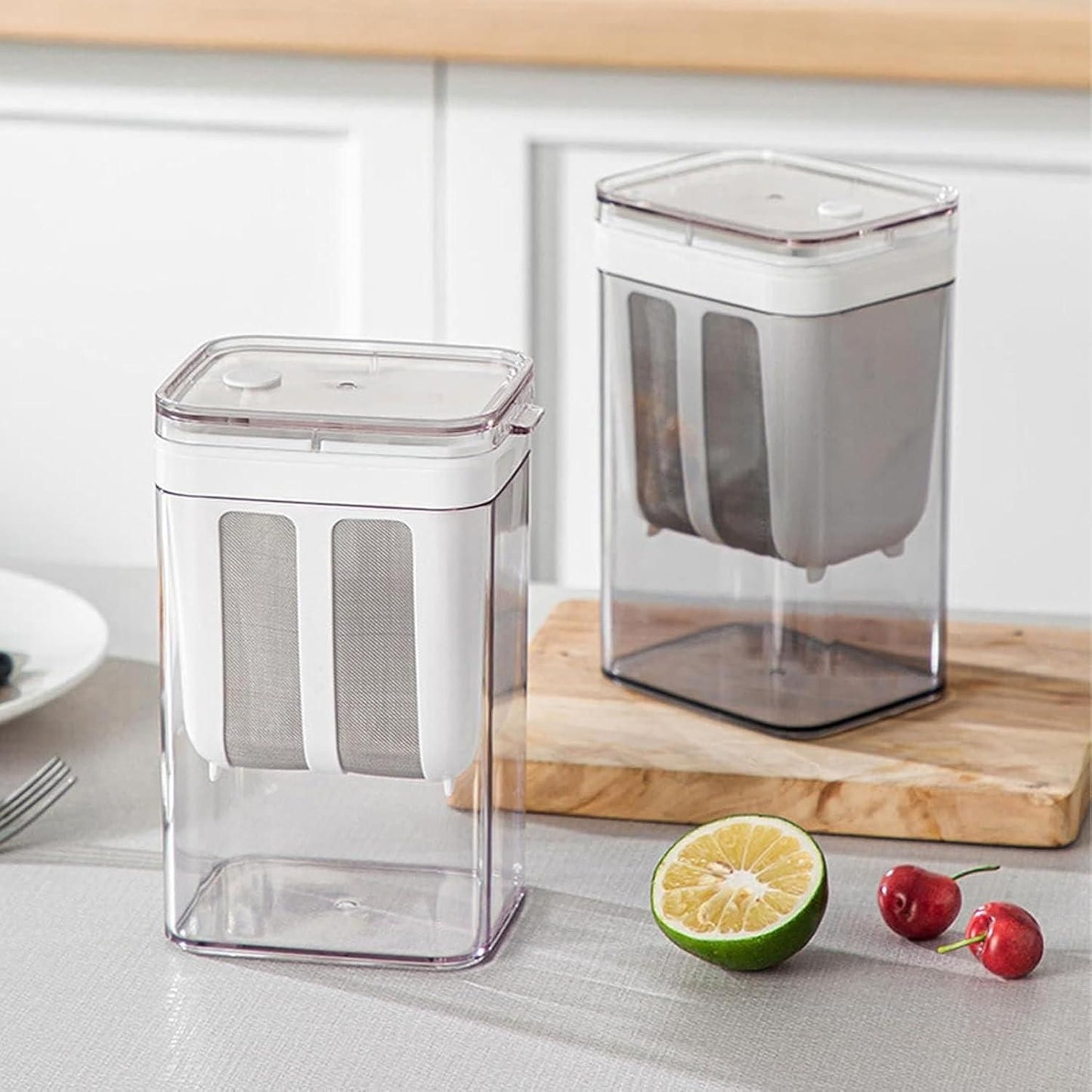 Clear plastic yogurt maker with strainer containers on kitchen countertop with lime and cherries