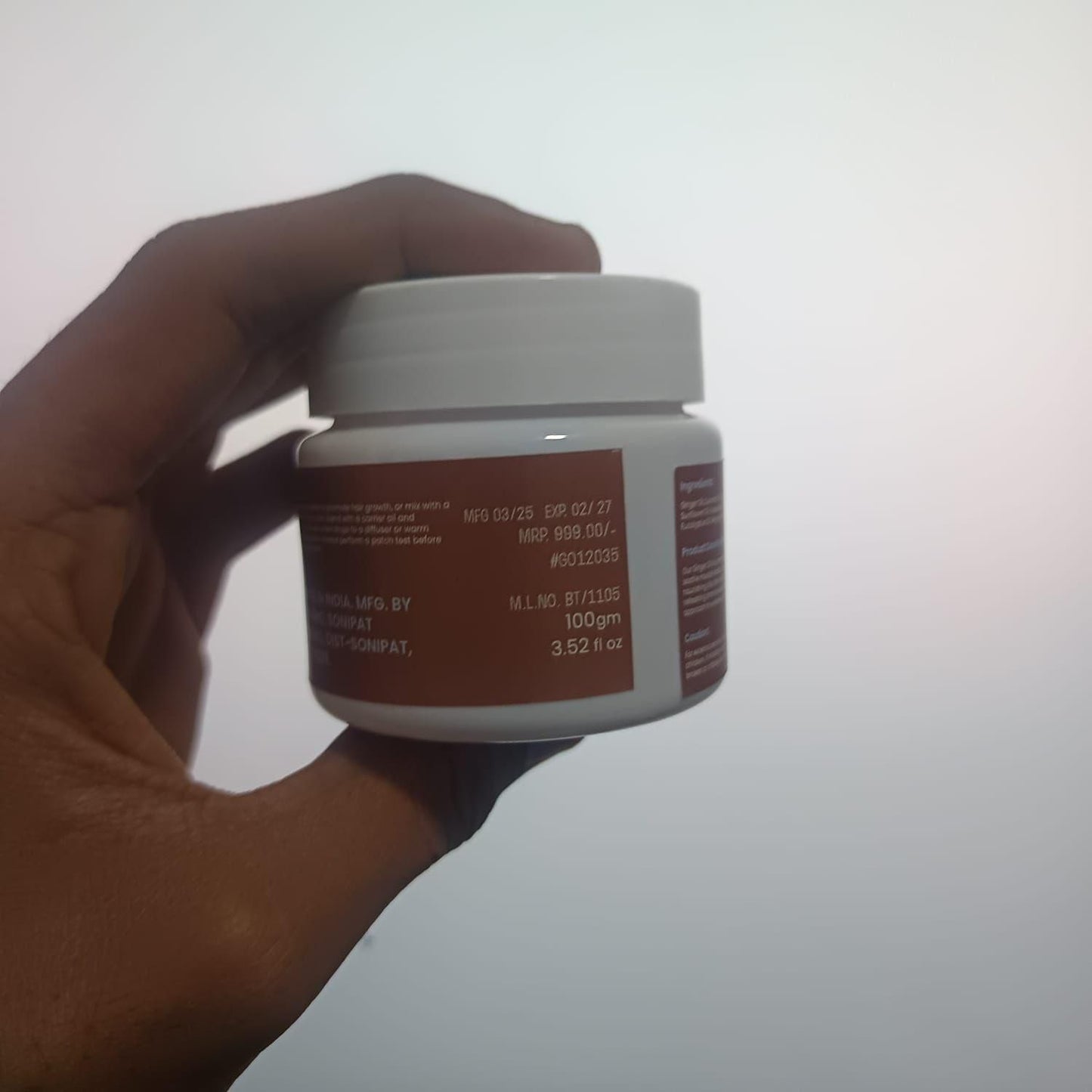 A hand holding a jar of ginger oil for body massage, showing the label and product details clearly