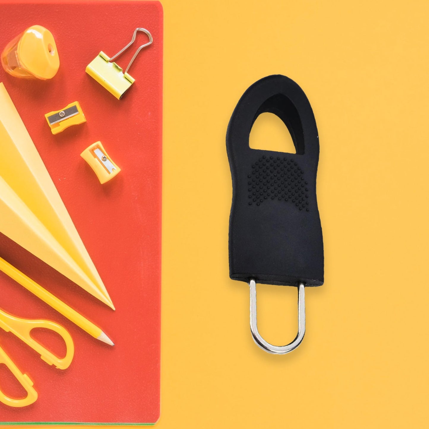 Zipper pull tab replacement tool in black next to stationery supplies on a bright background