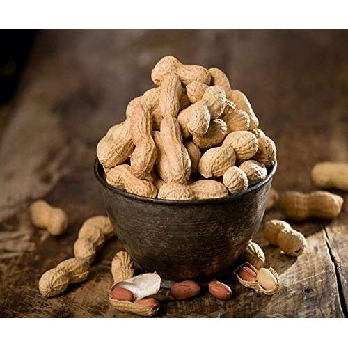 Bowl of organic raw groundnuts with whole and shelled peanuts on a rustic wooden surface