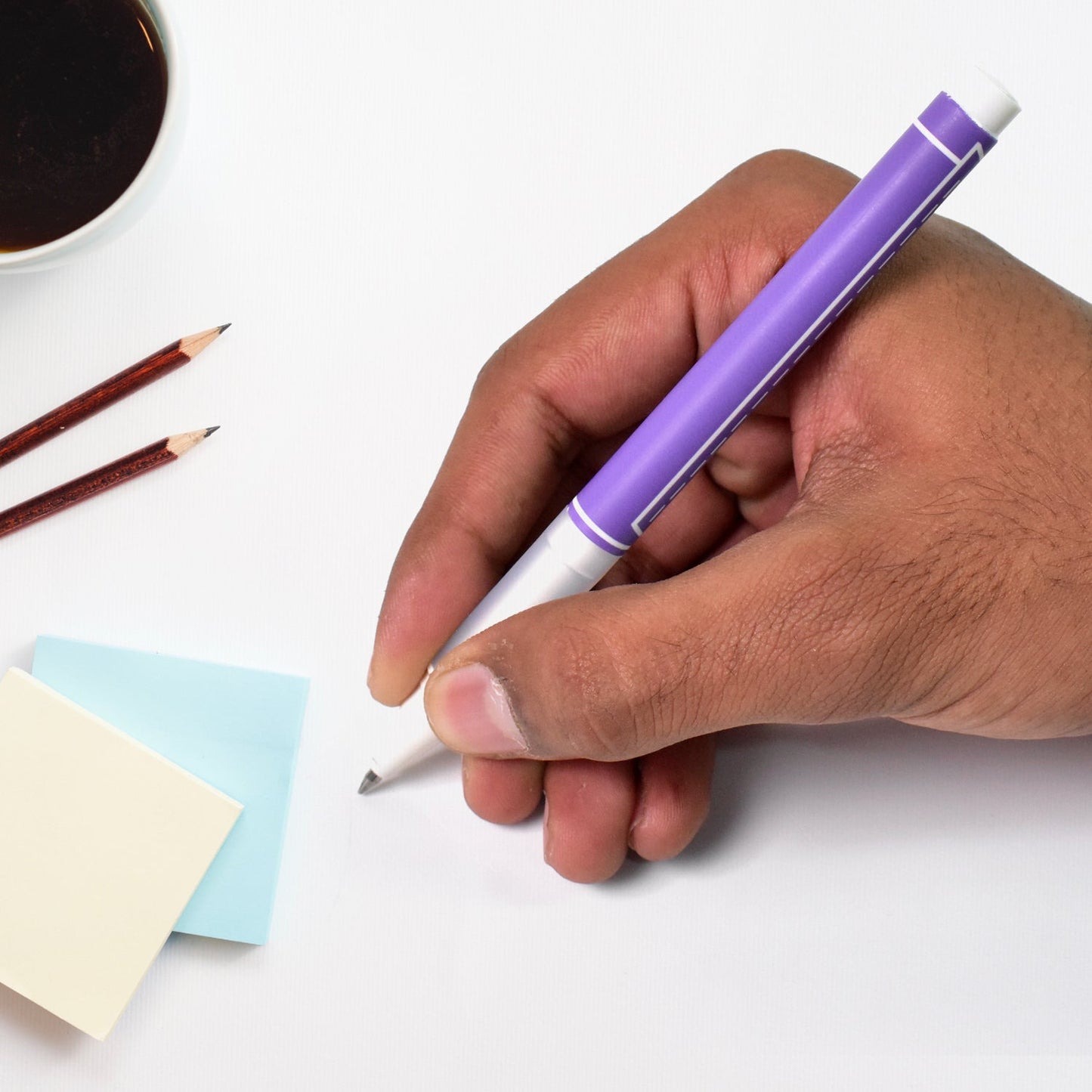 Hand holding a Your Brand 0.5 mm black ball pen over sticky notes and a coffee cup