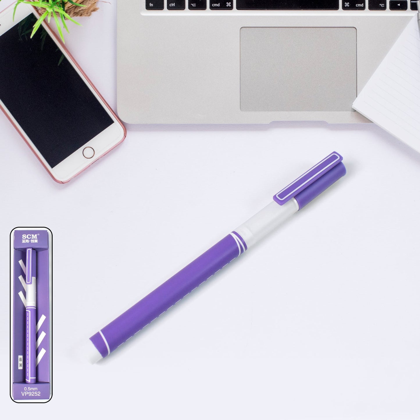 0.5 mm black ball pen in purple design placed next to a laptop and notebook on a desk