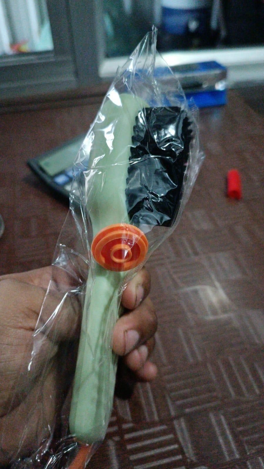 Multifunctional shoe brush with green handle and black bristles in clear plastic packaging