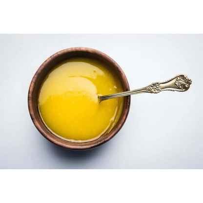 Golden A2 ghee in a wooden bowl with a silver spoon, perfect for cooking and healthy recipes