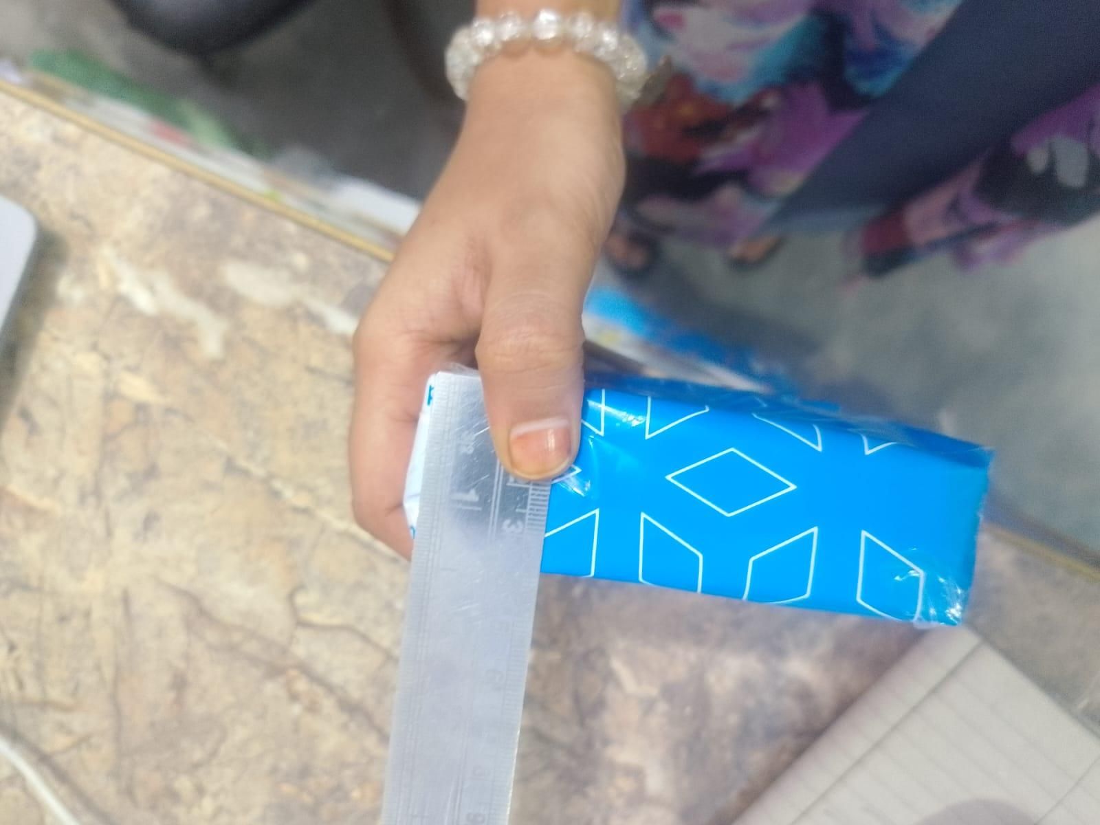 Hand holding a blue box while measuring with a ruler, featuring adhesive fabric fusion tape