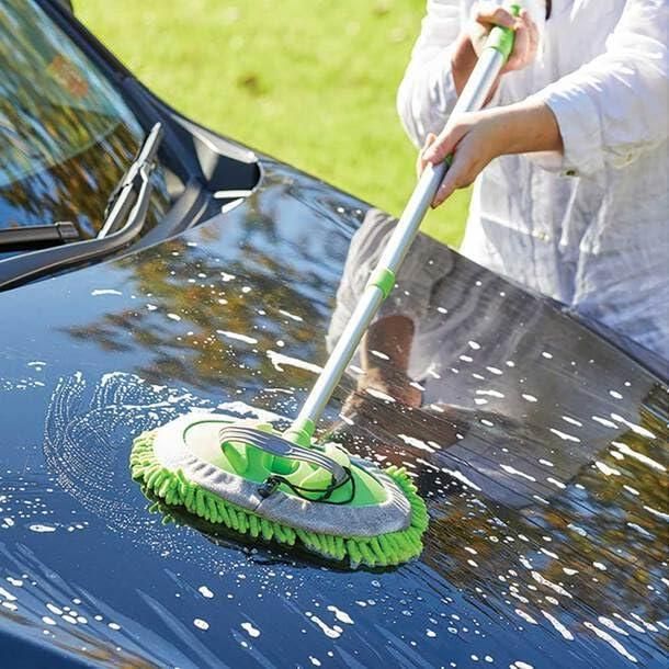Adjustable mop for outdoor use cleaning car hood with soap suds on a sunny day