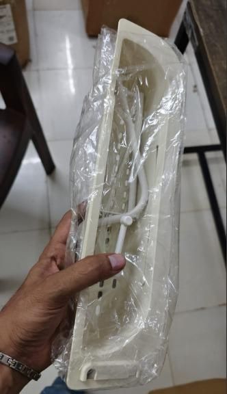 Hand holding a packaged adjustable sink organizer in a neutral color with drainage holes