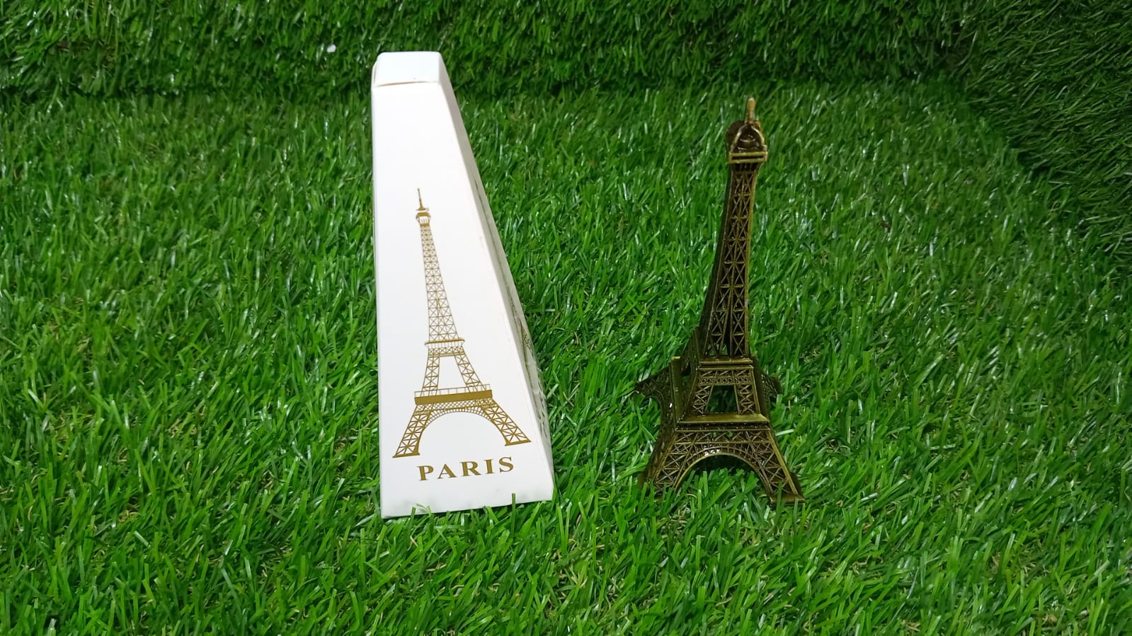 Antique Eiffel Tower statue displayed next to a Paris-themed box on green grass background