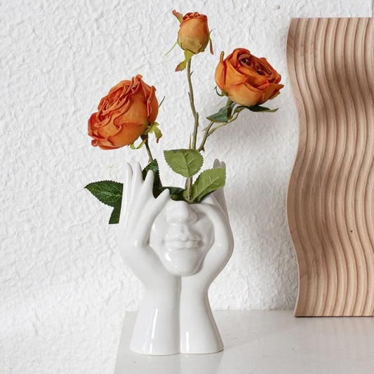 Artistic hand face vase for home decor with orange roses adding a vibrant touch