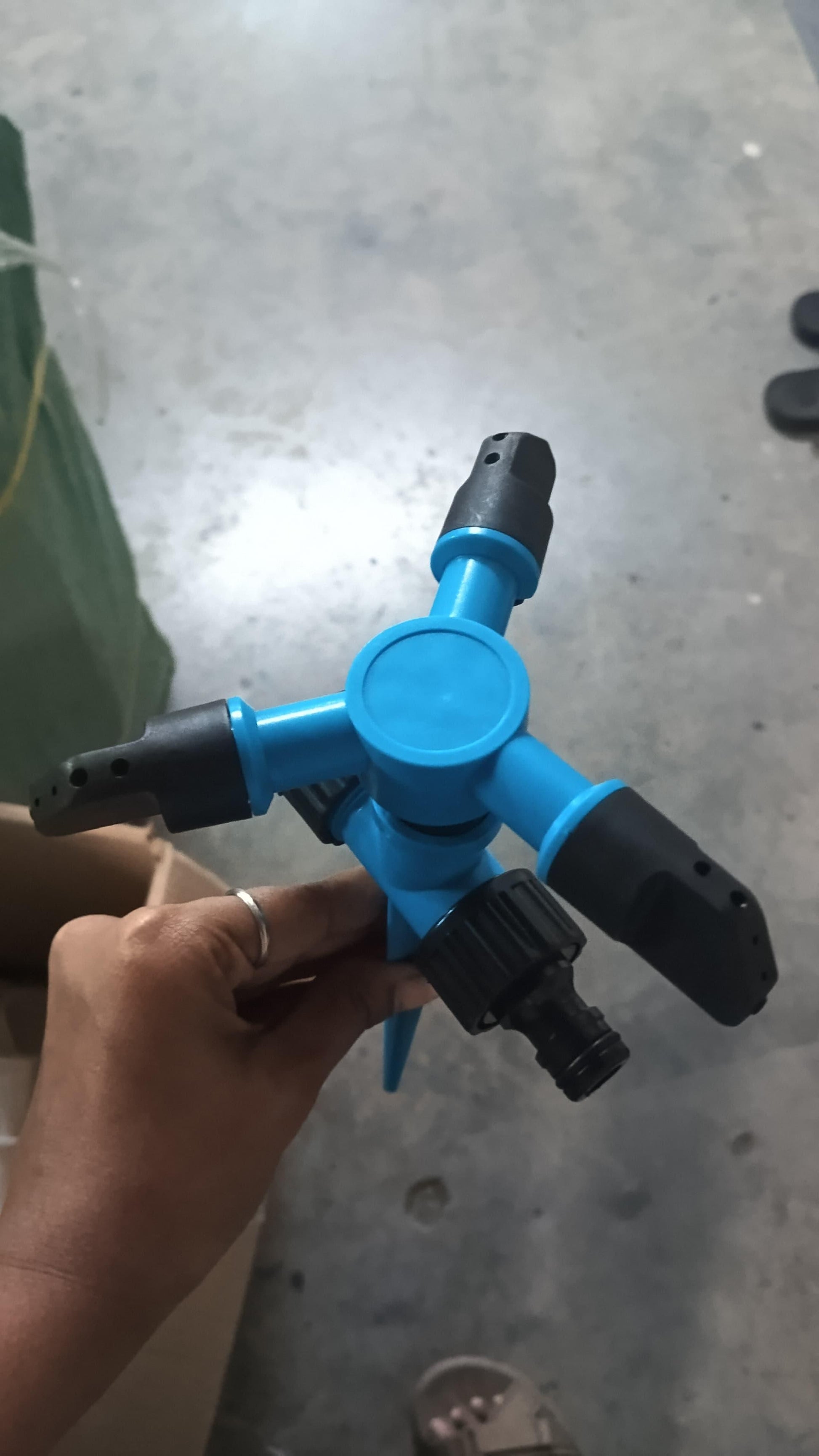 Blue THE GIR FARMER automatic rotating yard sprinkler with three black adjustable nozzles held in hand