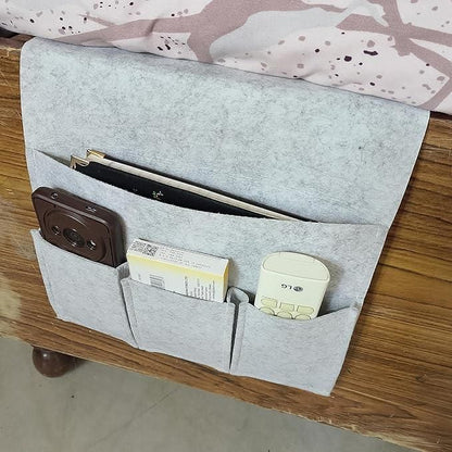 Gray bedside pocket organizer for essentials holding remote controls, books, and a small box on wooden surface