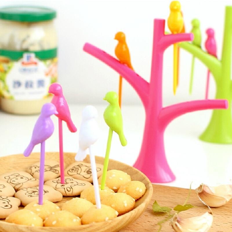 Colorful bird fruit fork for kids displayed on a playful tree stand with snacks