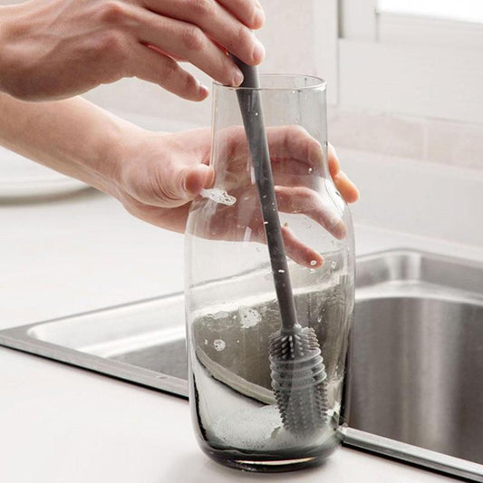 Hand using a bottle cleaning brush to scrub a glass bottle in a modern kitchen sink