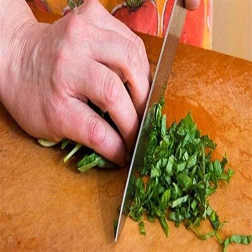 Closeup of hand chopping fresh herbs on a wooden chopping board with knife set on a kitchen countertop