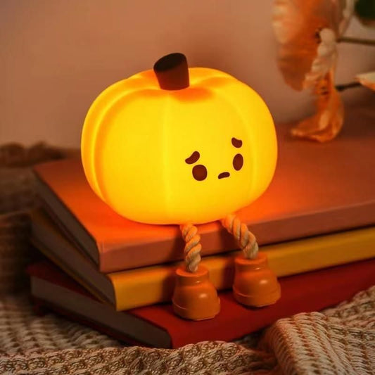 Cute pumpkin-shaped touch control silicone lamp with expressive face sitting on stacked books