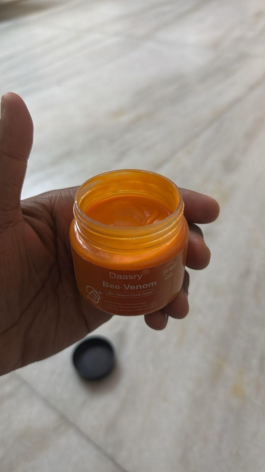 Dassry bee venom skin cream in an orange jar held in a hand, showcasing its rich texture