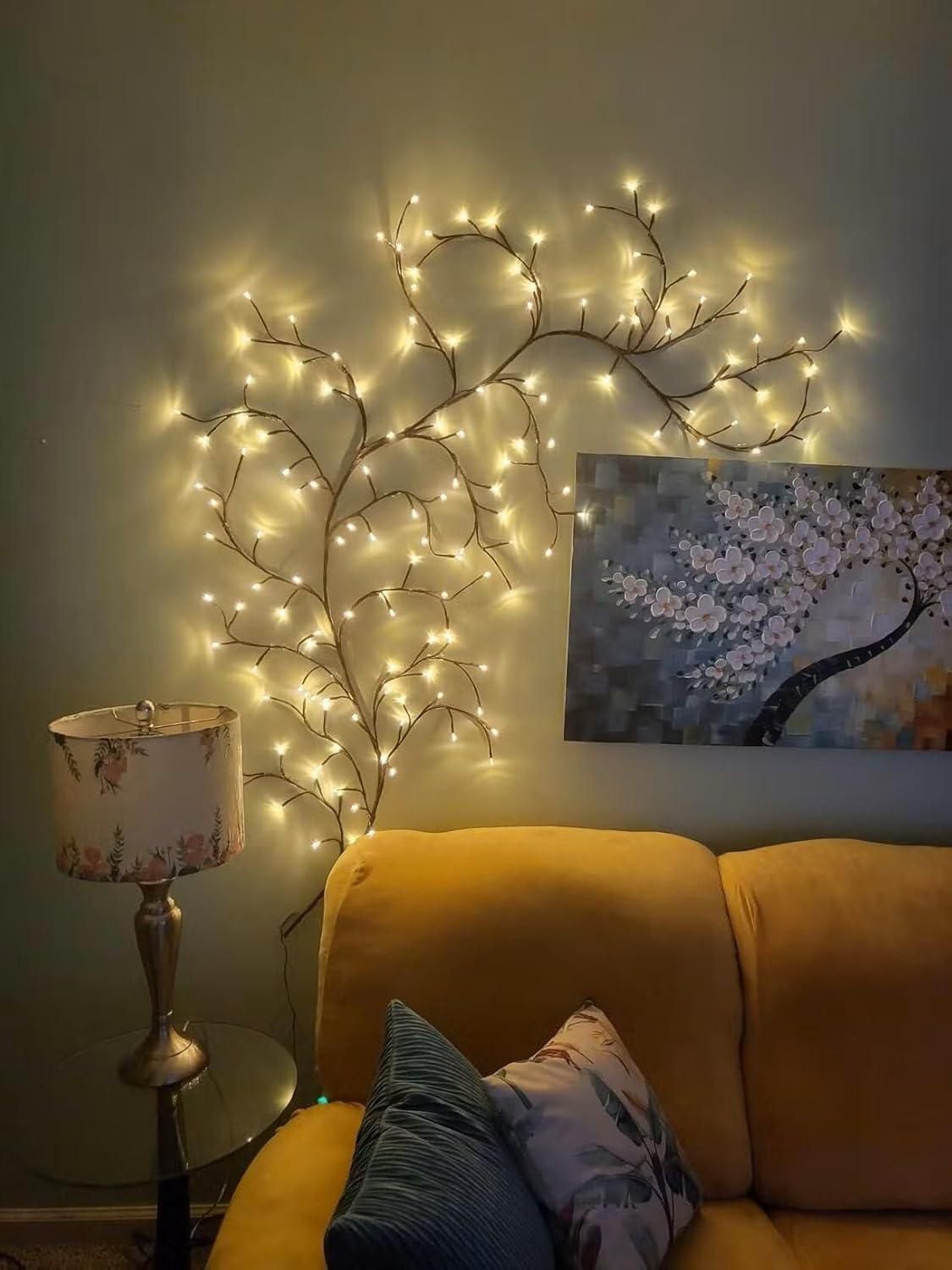 Decorative branch fairy lights illuminated on a wall with a cozy yellow couch and floral lamp