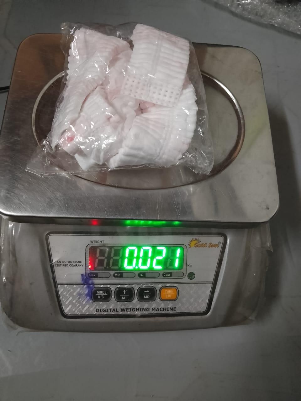 Digital weighing machine displaying 0.021 kg with packaged disposable pillowcase on the scale