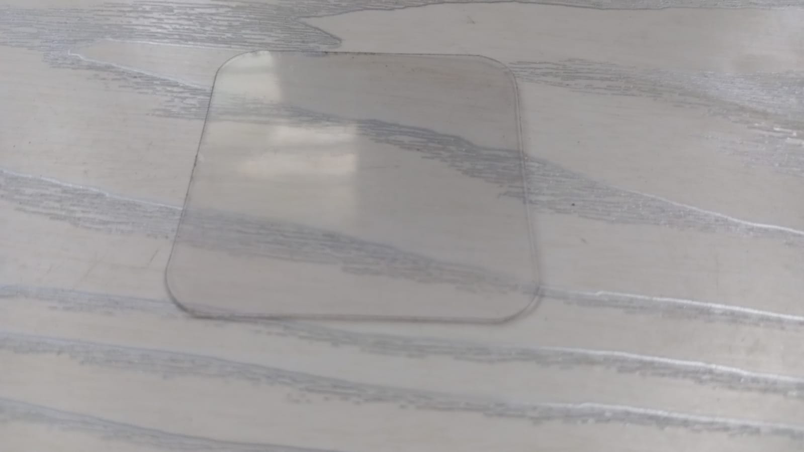 Clear square piece of double-sided nano adhesive tape on a wooden surface for versatile bonding solutions