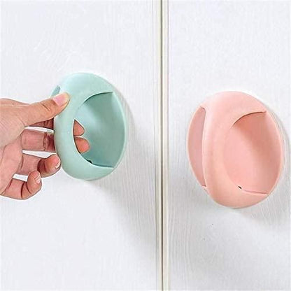 Pastel mint and pink oval adhesive handles for cabinets stuck on white doors with hand pulling green handle