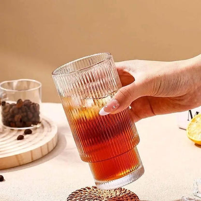 Product image of a ribbed clear glass filled with iced tea held by hand glass tumbler with wood cap nearby