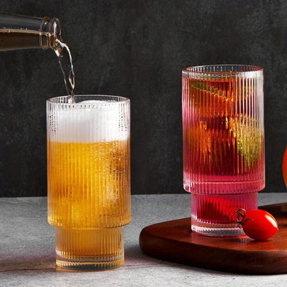 Two ribbed glass tumblers on a table one being filled with beer the other with a red cocktail product glass tumbler with wood cap