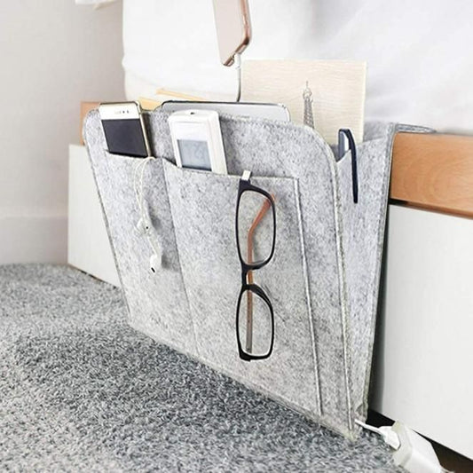 Gray felt bedside pocket for essentials hanging on bed frame holding phone glasses and remote