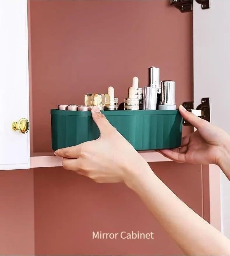 Green drawer organizers for makeup being placed inside a pink mirror cabinet holding various cosmetic bottles