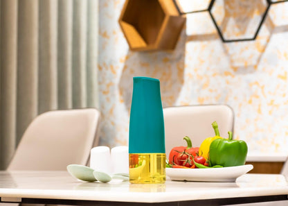 Teal top and clear yellow oil dispenser bottle for kitchen on table with plate of peppers and tomatoes