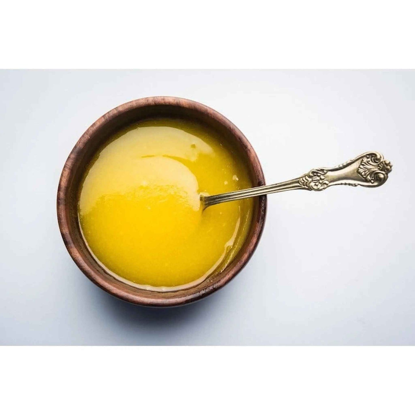 Rich and creamy Gir Cow Ghee in a wooden bowl with a silver spoon, perfect for cooking and baking.
