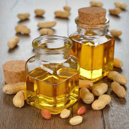 Bottles of organic ground nut oil surrounded by shelled peanuts on a wooden surface