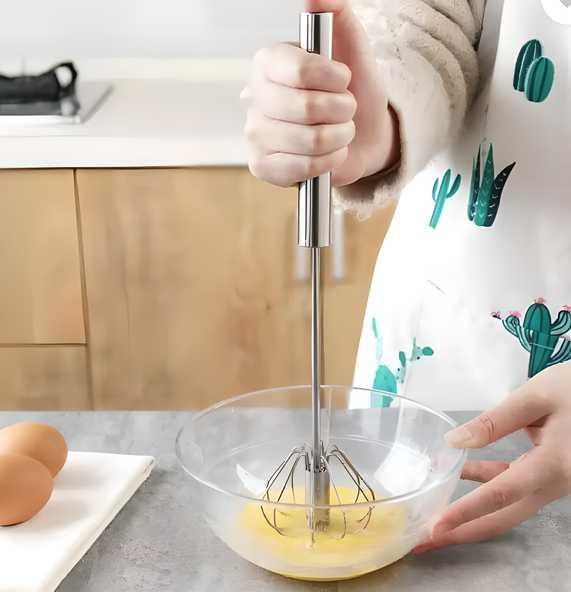 Hand whisk mixer for baking in use whisking eggs in a clear bowl on kitchen counter