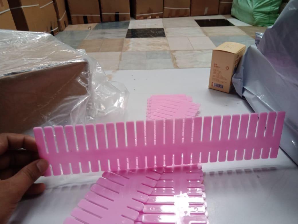 Pink plastic adjustable drawer organizer dividers slotted panels held by hand on packing table