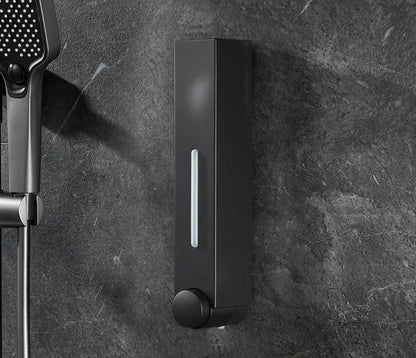 Matte black wall mounted soap dispenser with clear level window and round pump knob next to handheld shower head