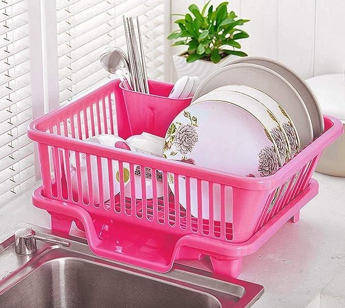 Pink compact plastic dish drainer with cutlery holder on countertop holding floral plates and utensils