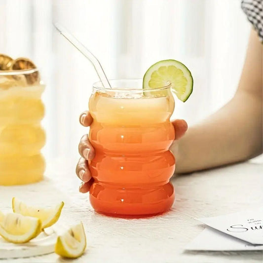 Hand holding wave shape glass with wood cap filled with layered orange drink straw and lime garnish