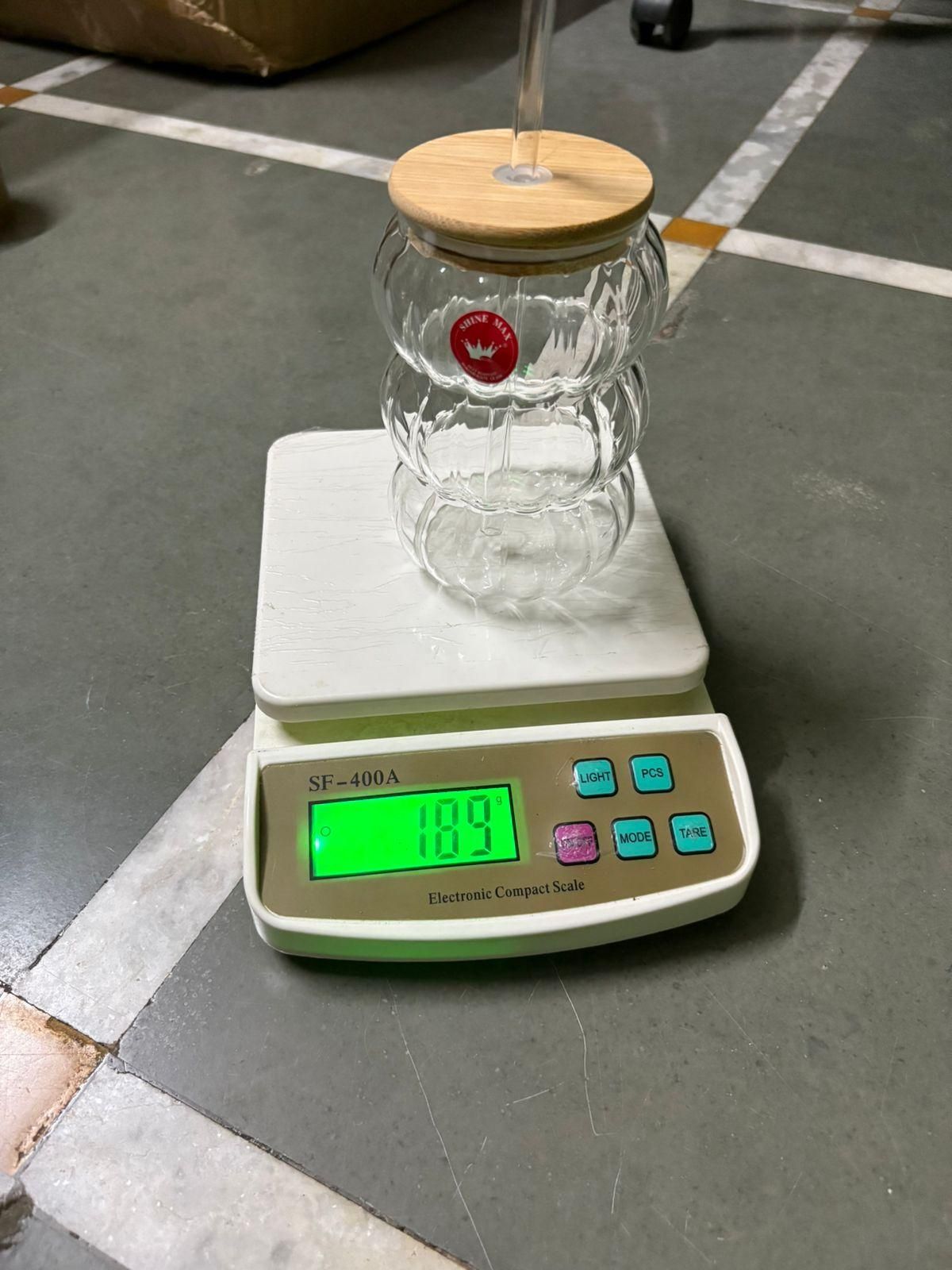 wave shape glass with wood cap and straw placed on a digital kitchen scale reading 189 g on concrete floor