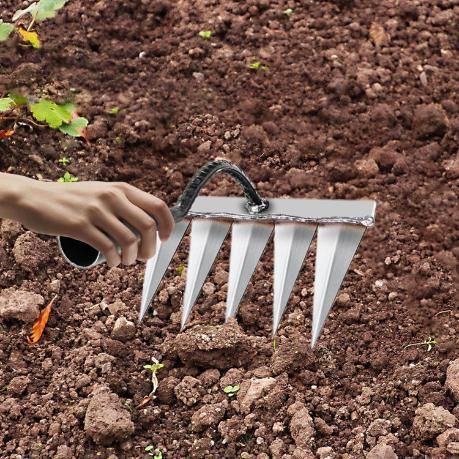 Manual tool for removing weeds with metal spikes held over soil to clear garden area
