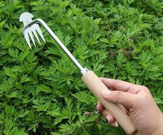 Manual weed remover for small farms with wooden handle and metal prongs held above green plants