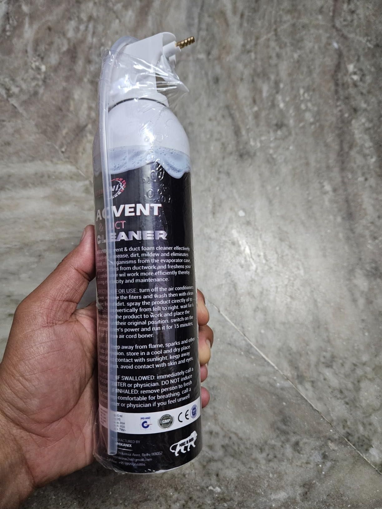 Hand holding foaming AC vent cleaner for home in a white spray can with black label against a gray textured background