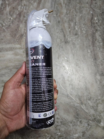 Hand holding foaming AC vent cleaner for home in a white spray can with black label against a gray textured background