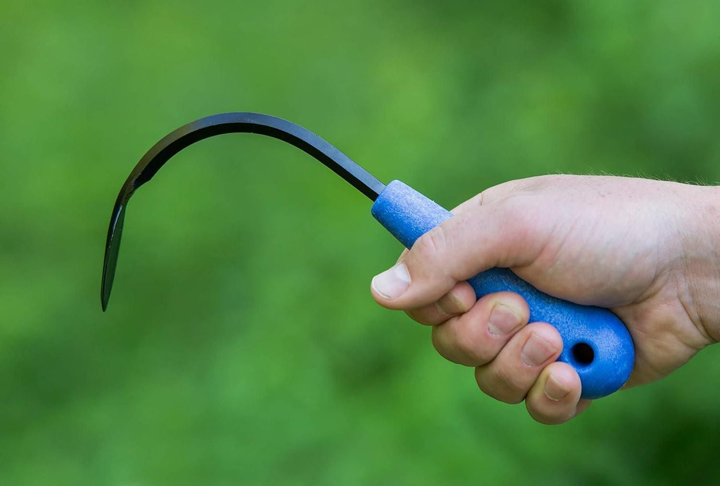 Hand holding a blue-handled mini weeder from the mini weeder pack for raised beds against green background