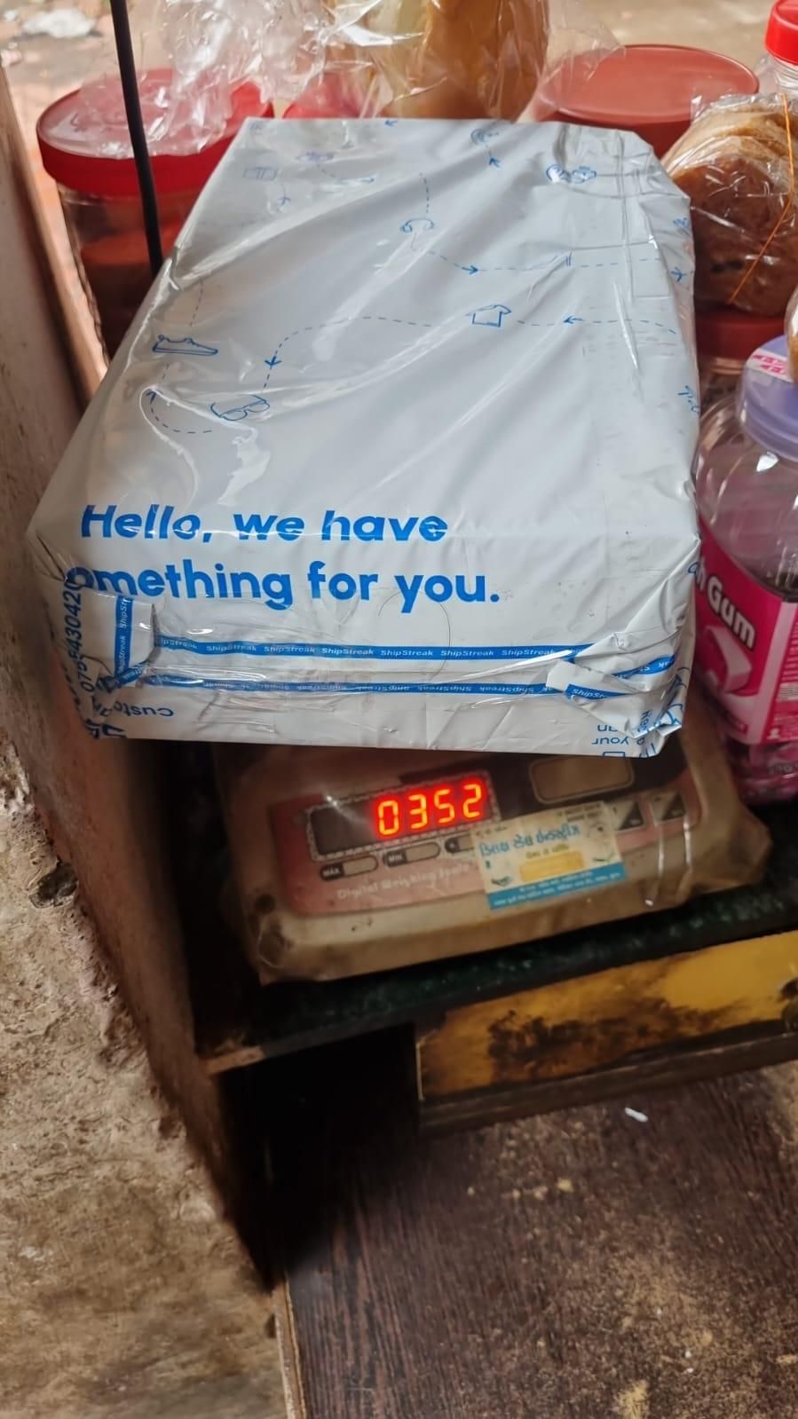 Package wrapped in plastic with blue text Hello we have something for you placed on a weighing scale showing 0352