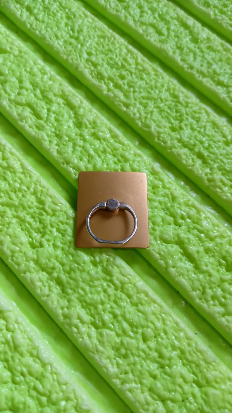 Gold mobile phone finger stand grip on a textured green background for easy device handling