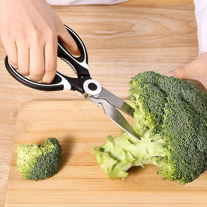 Hands using multi function kitchen scissors to cut fresh broccoli on a wooden cutting board
