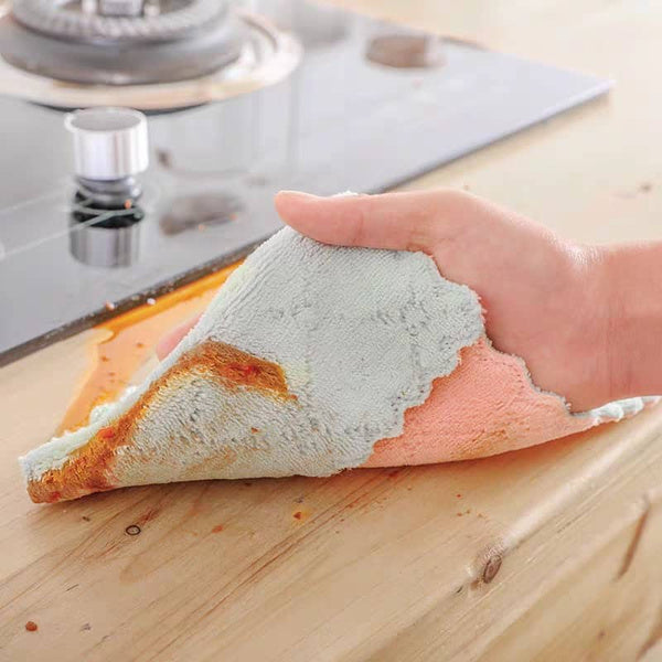 Hand using a multi-purpose kitchen wash towel to clean a spill on a wooden countertop