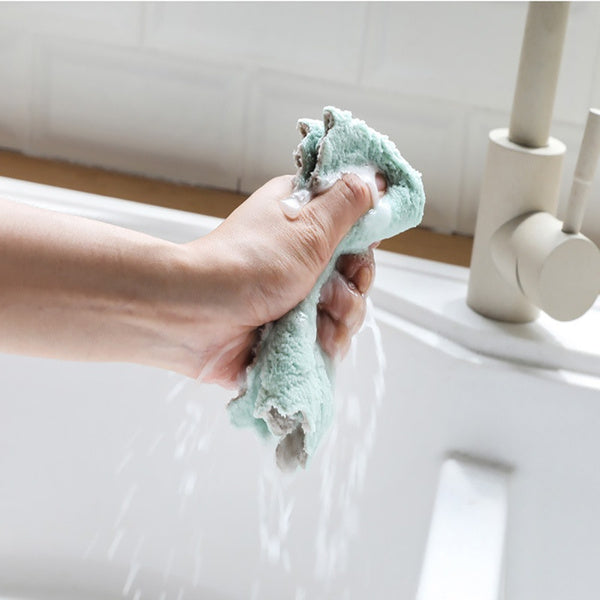 Hand squeezing a damp multi-purpose kitchen wash towel in a clean sink for efficient cleaning